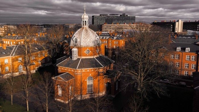 Historisk kuppelkirke omgivet af rødstensbygninger og nøgne vintertræer under en overskyet himmel.