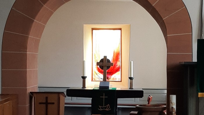 Ein ruhiger Kirchengang mit einem Altar, der Kerzen, ein Kruzifix und einen roten Stoffhintergrund aufweist.