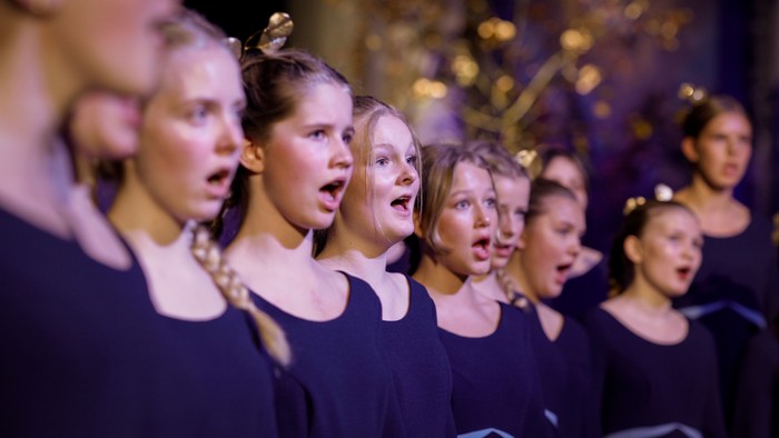 En gruppe børn synger i kor, alle med mørkeblå tøjer og nogle med hårbånd.