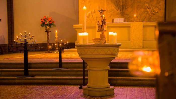 Brennende Kerzen auf Taufstein und Altar während einer Taizé-Andacht
