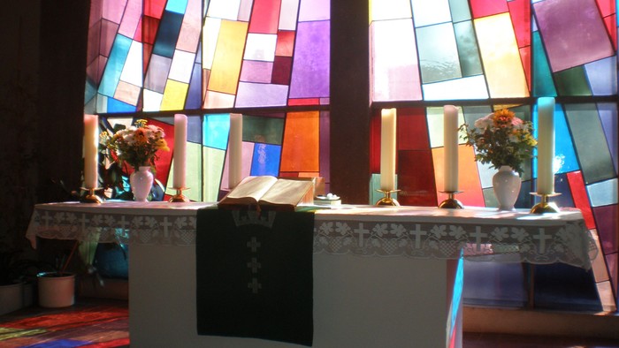 Bunte Kirchenfenster erleuchten den Altar mit Blumen und Kerzen