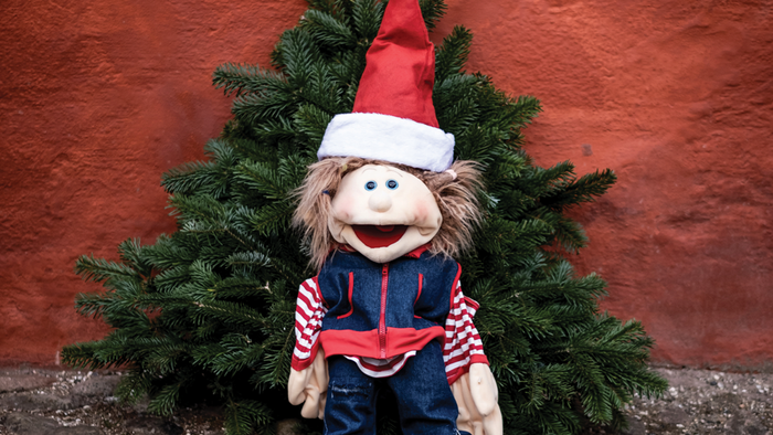 En lille nisse med juleskæg og hat sidder foran en lille julenæd.