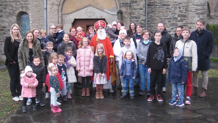 Eine Gruppe von Erwachsenen und Kindern posiert mit einem Mann im Weihnachtsmannkostüm vor einem steinernen Gebäude.