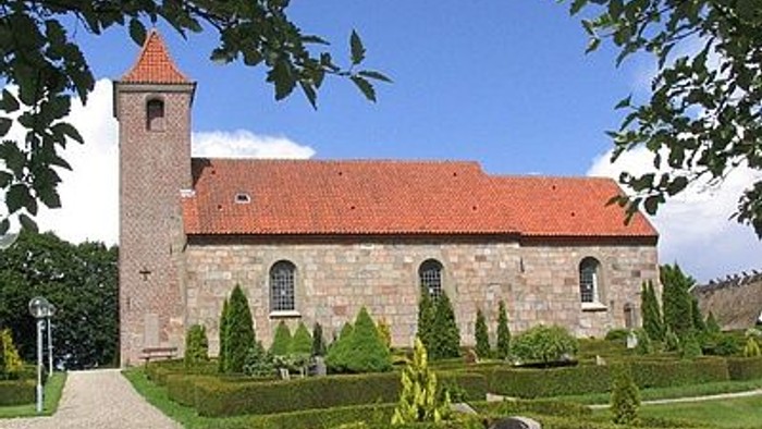 En kirke med klokketårn og en have med træer og buske