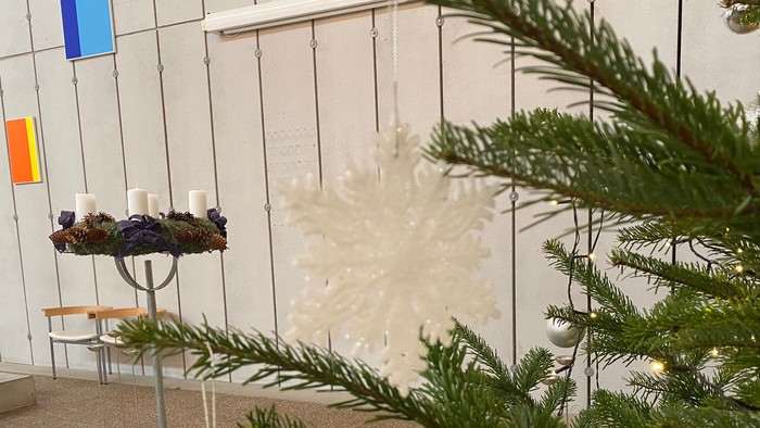 En juletree med pynt og en kande med lys på en bord.