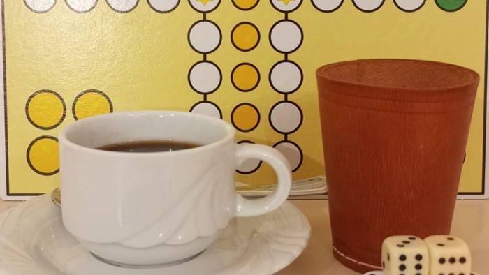 Bunte Figuren, Würfel und Kaffeetasse vor einem Spielbrett