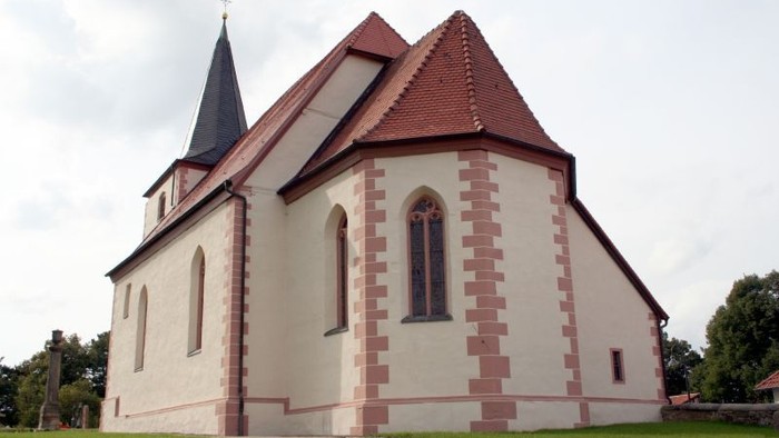 Kleine weiße Kirche mit rotem Zickzackmuster und schwarzem Turm auf grünem Rasen
