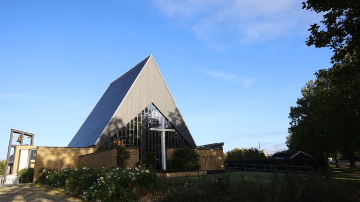 Moderne trekantet kirke med store glasvægge placeret i et roligt, anlagt udendørsområde.