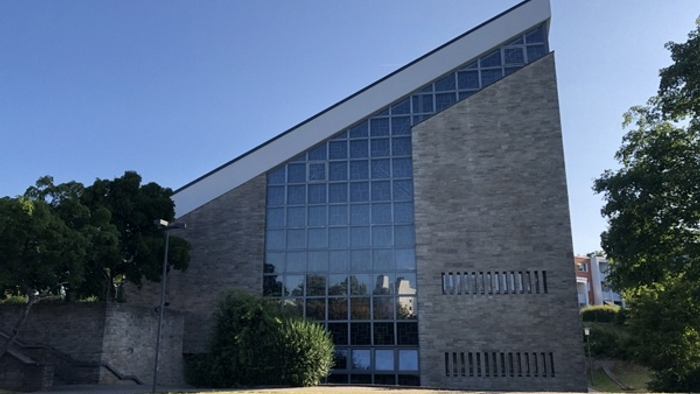 Modernes Gebäude mit großen Glasfenstern und Treppe, umgeben von Bäumen und Gras.