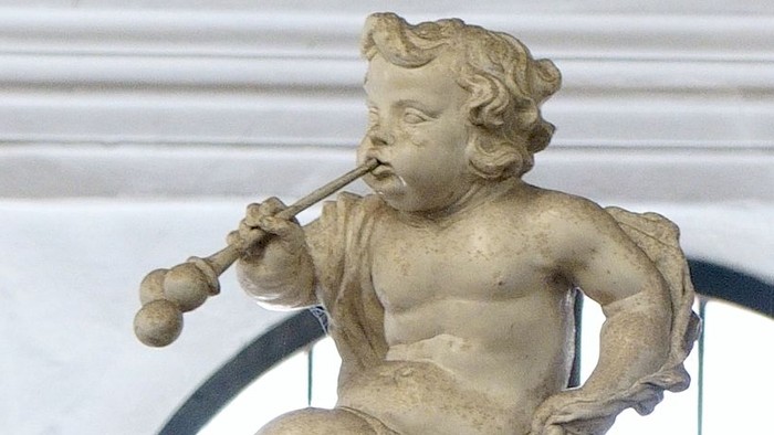 Die Statue eines Kindes, das eine Flöte spielt, vor einem weißen Gebäude.