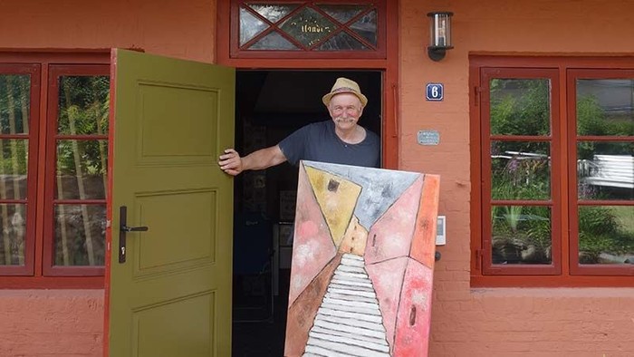 Mann steht in Tür eines roten Hauses mit buntem Wandgemälde.