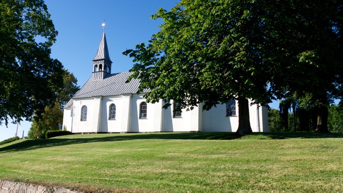 Hvid kirke på grøn græsplæne omgivet af grønne træer