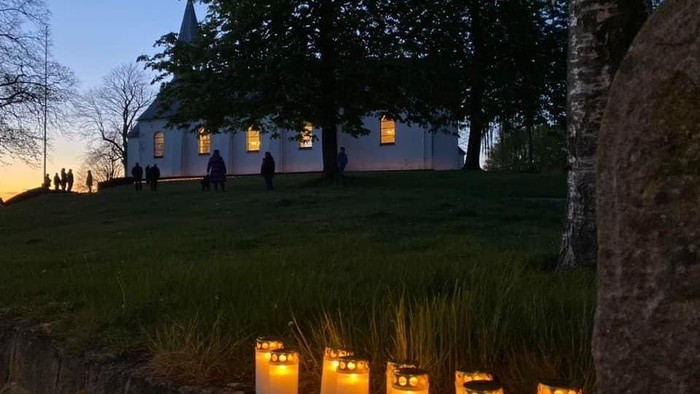 Tusmørke. Levende lys foran hvid kirke med lys i vinduerne. 