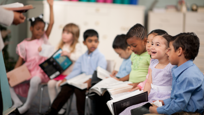 Kleinkinder sitzen in einer Reihe mit einer Bibel in der Hand.