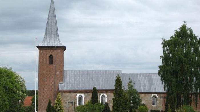 En kirke med tårn og spire, omgivet af træer og buske