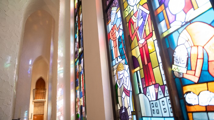 Lebendiges Buntglasfenster mit farbenfrohen religiösen Szenen in einem gewölbten architektonischen Rahmen.