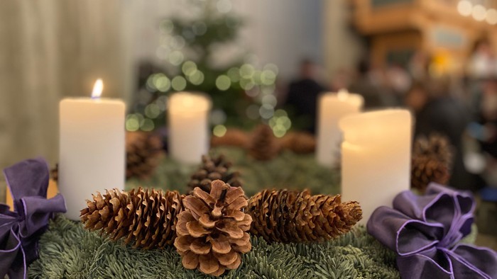 Lys og kogler på grønt med lilla bånd, juletræ i baggrunden