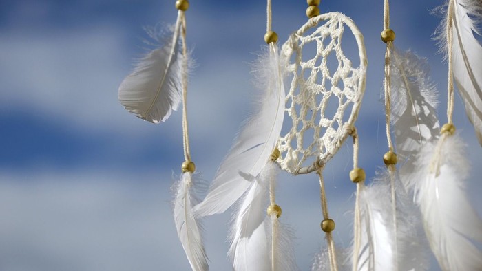 Weißer Traumfänger mit Federn vor blauem Himmel