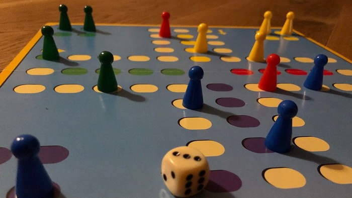 Ein Brettspielaufbau mit bunten Spielfiguren und einem Würfel auf einem blauen Spielbrett.