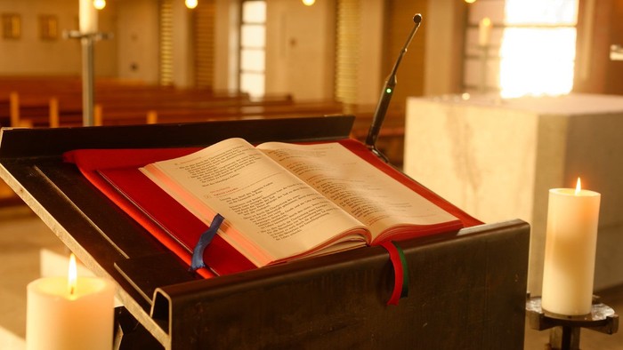 Offene Bibel auf Lesepult in Kirche mit brennenden Kerzen