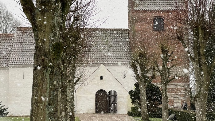 En snødekkede kirke med tårn og træer.