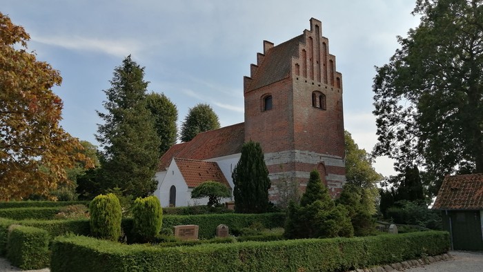 En gammel kirke med tårn og omgivelser med buske og træer