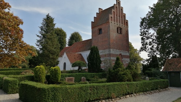 En gammel kirke med tårn og omgivelser med buske og træer