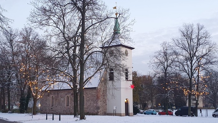Schneebedeckte Straße mit Kirche, Autos und Bäumen mit Lichtern