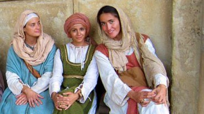 Drei Frauen in traditioneller Kleidung posieren vor einer Steinmauer