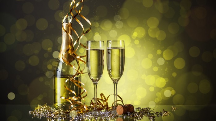 To skålene og flaske med champagnet, pyntet med guldfarvet konfetti og bælter, foran glitrende baggrund