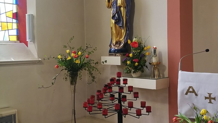 In der Kirche steht eine Statue der Jungfrau Maria mit Blumen und Kerzen.