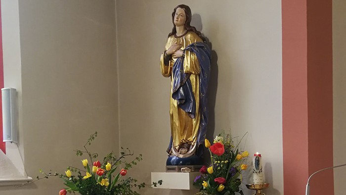 In der Kirche steht eine Statue der Jungfrau Maria mit Blumen und Kerzen.