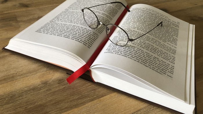 Ein offenes Buch mit einer Brille, die auf einem roten Lesezeichen liegt.