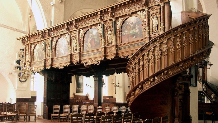 Prächtige, verzierte Holztreppe in einem großen, hellen Raum mit hohen Decken und Kronleuchtern.