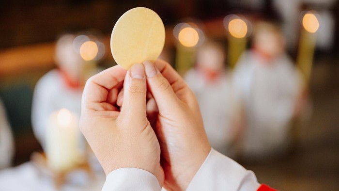 Eine Person in liturgischer Kleidung hält eine Hostie während einer religiösen Zeremonie.