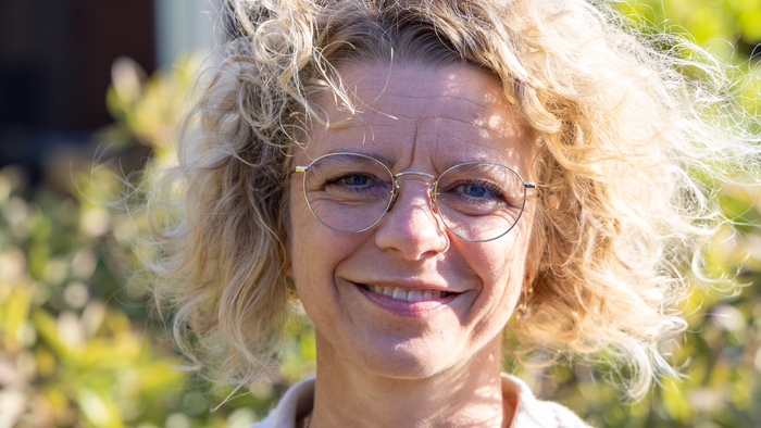 En kvinde med kurve hår og briller smiler til kameraet.