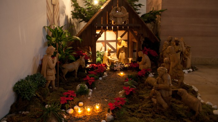 Eine Weihnachtskrippe mit Figuren und beleuchtetem Stall, umgeben von Kerzen und Weihnachtsdekorationen