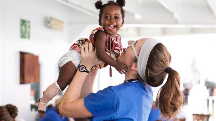 En kvinde fra Mercy Ships løfter en lille afrikansk pige