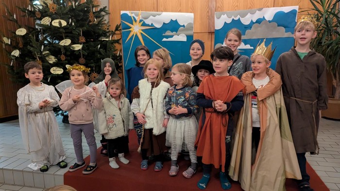 Kinder in Kostümen stehen vor Weihnachtsdekoration