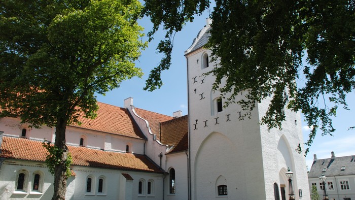 Et stort, hvide kloster med spisse tak og en høj tårn, omgivet af træer og græsplæne
