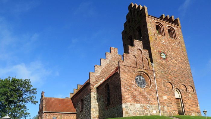 En middelalderkirke med tårn og gravsteder på en grøn bakke