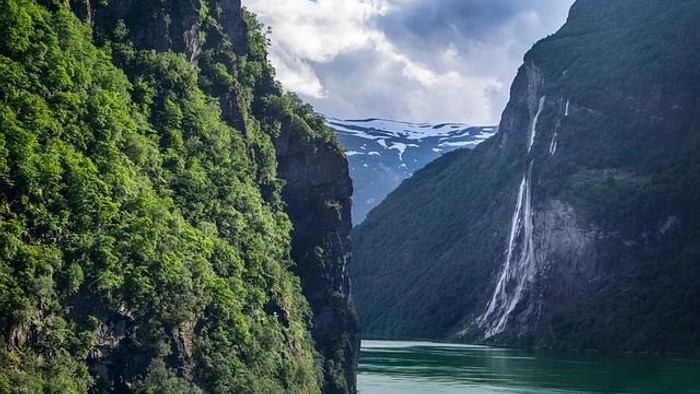 Ein tiefes, grünes Tal mit einem Fluss und steilen, bewaldeten Hängen unter einem bewölkten Himmel