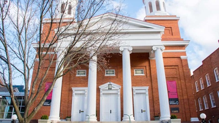 Das Bild zeigt eine rote Backsteinkirche mit weißen Säulen und Treppe.