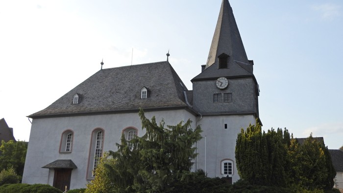 Kirchengebäude mit Uhrturm und grünem Gestrüpp