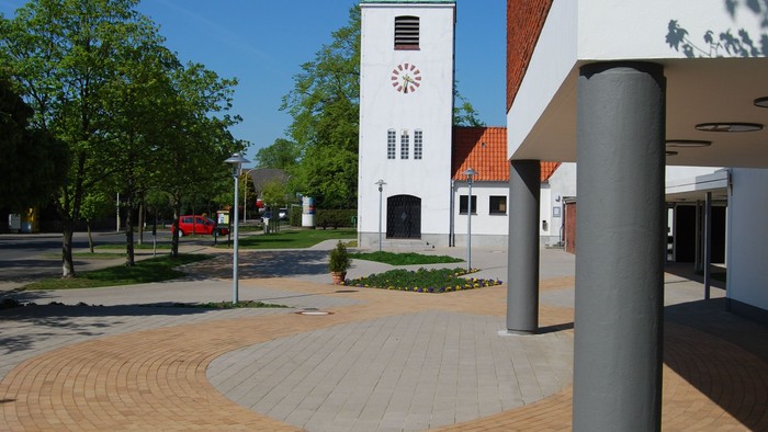 Buntes Kopfsteinpflaster, Kirche mit grünem Turm, grauer Pfahl