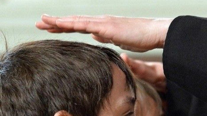 Eine Hand wird auf den Kopf einer Person gelegt.