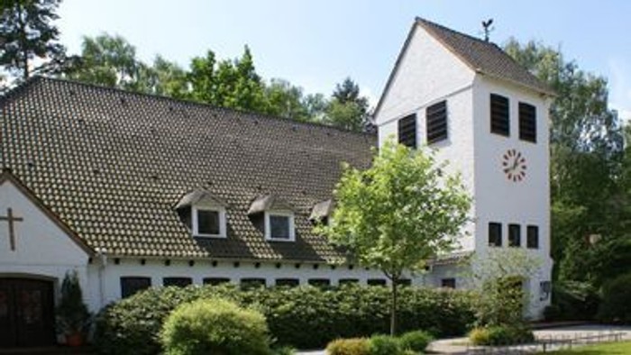 Das Bild zeigt ein weißes Haus mit dunklem Dach und einem Garten.