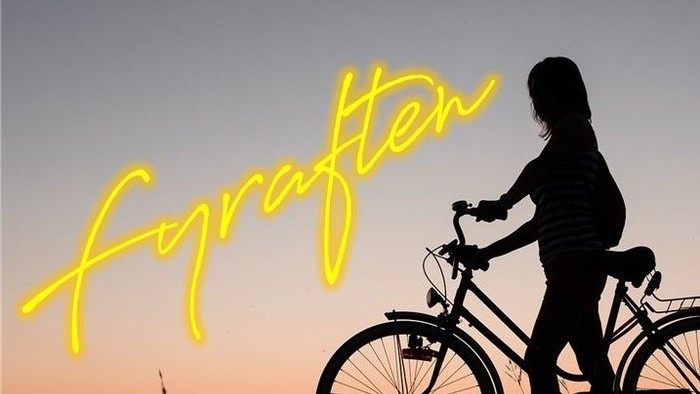 En kvinde cykler forbi et lille hus med klokketårn ved solnedgang