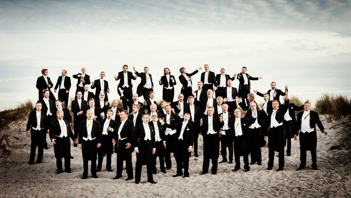 En gruppe mænd i formelle klæder står på en sandstrand