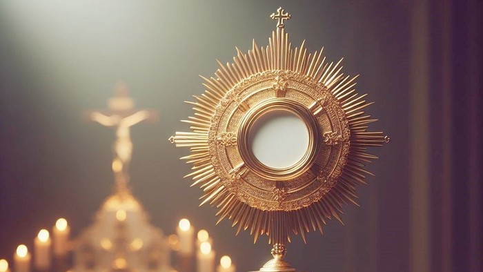 Goldene Monstranz auf einem Tisch mit brennenden Kerzen und einem Kruzifix im Hintergrund.